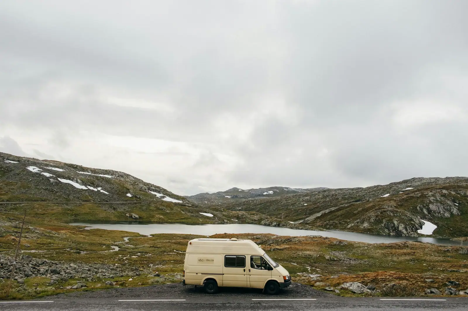 Camper blanca aparcada en una carretera que cruza una meseta abierta del norte, con un lago y colinas bajas