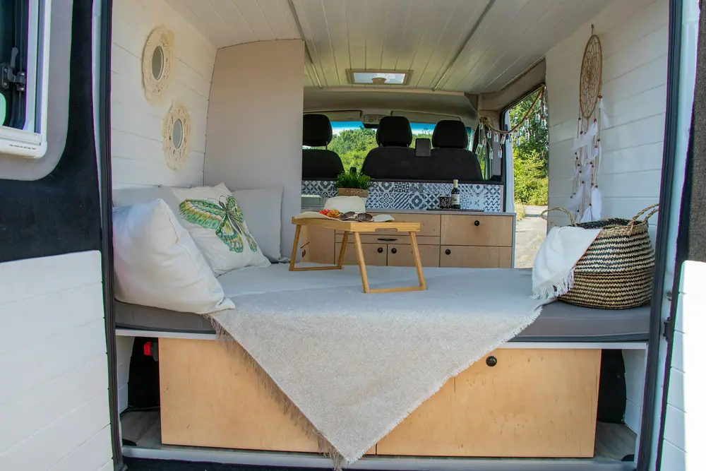 Cama hecha en una camper con cajones de madera bajo la base