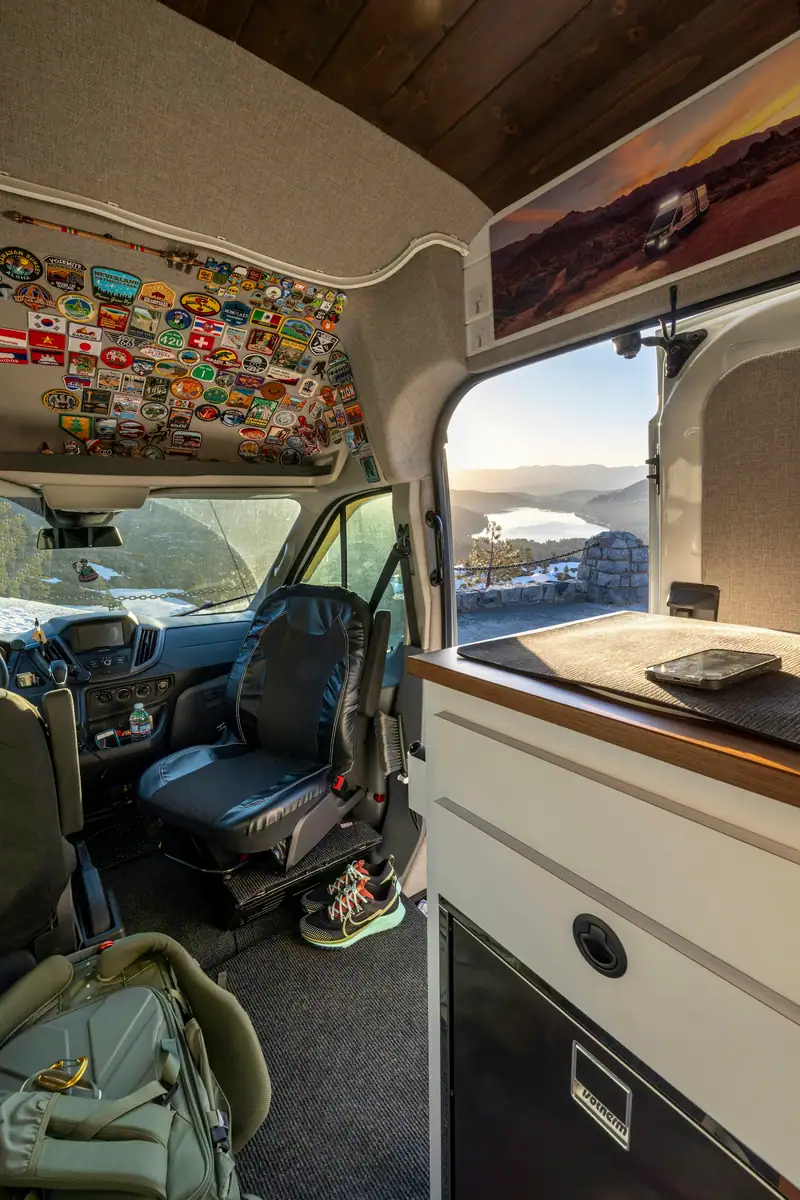 Asiento del conductor girado en la cabina de una camper, con la puerta lateral abierta y vistas a un lago