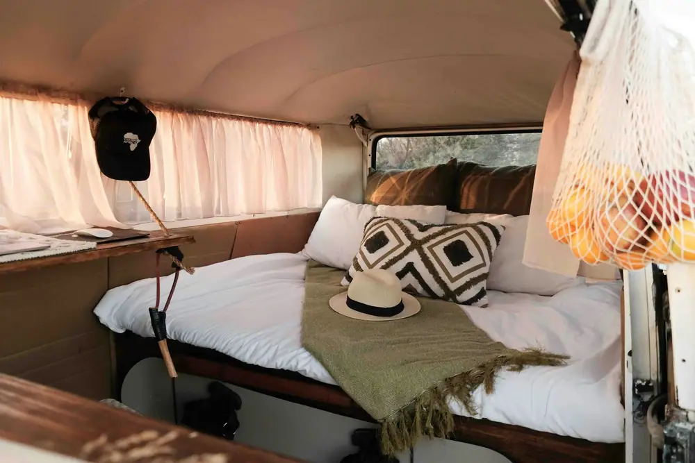 Zona de cama de una camper con una bolsa de malla colgada de la pared y un sombrero en un gancho
